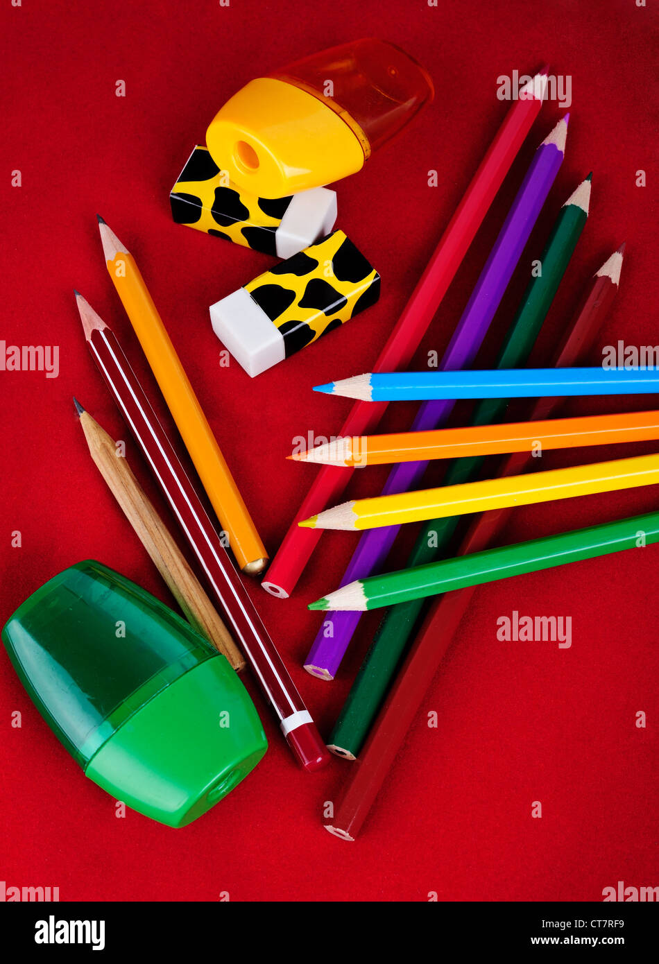 Colored pencils, erasers, sharpeners isolated on red background Stock