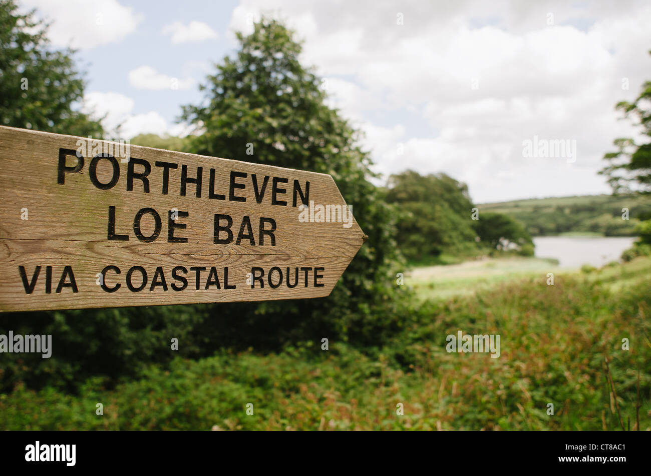 A wooden sign with directions for Porthleven and Loe Bar, Cornwall located in the Penrose Estate on an overcast day with Loe Pool in the background Stock Photo