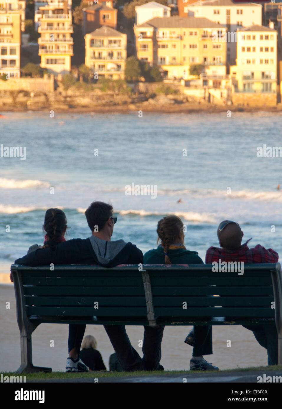 Two women and two men in early 20s on bench overlooking Bondi Beach at sunset Sydney New South Wales Australia Stock Photo