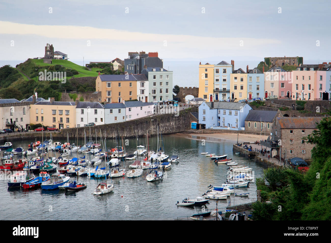 Tenby Harbour at high tide with boats overlooked by colourful painted Regency houses and castle at dusk. Stock Photo