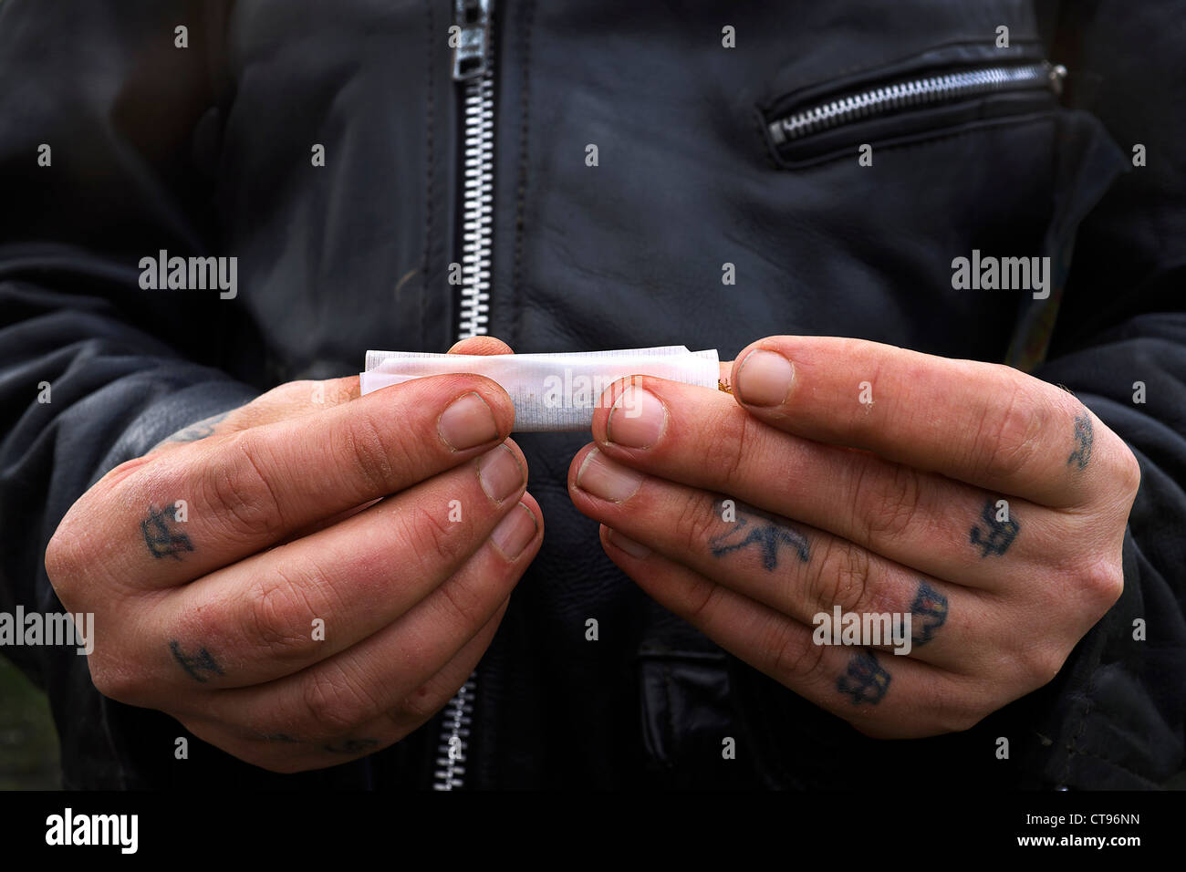 Close up of two hands with tattoos on the fingers rolling a cigarette using loose tobacco, Govan, Glasgow, Scotland, UK Stock Photo