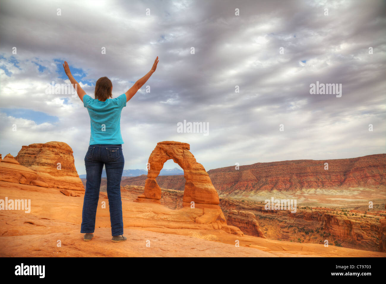 Woman with raised hands staying in front of Delicate Arch, Utah Stock Photo