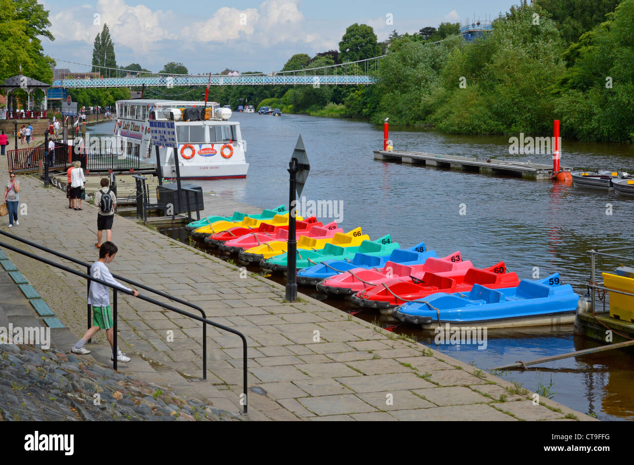 Summer view of white sightseeing tour boat on the River Dee at Chester colourful peddle boats at riverside moorings suspension bridge Cheshire England Stock Photo