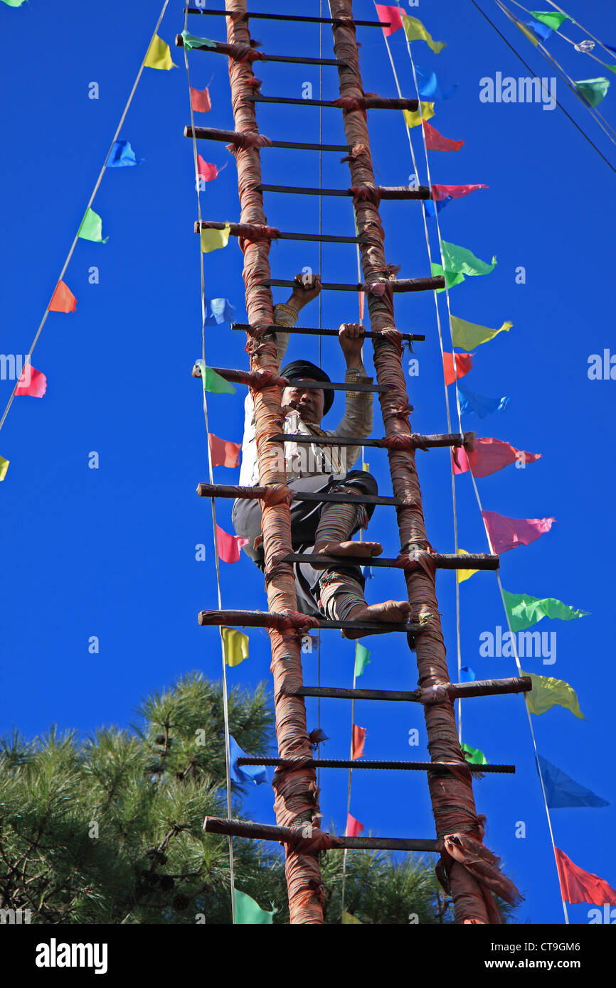 A barefooted Naxi ethnic man climbs the steps of a ladder made of sharp knives at the Dongba Valley Cultural Village in Lijiang Stock Photo