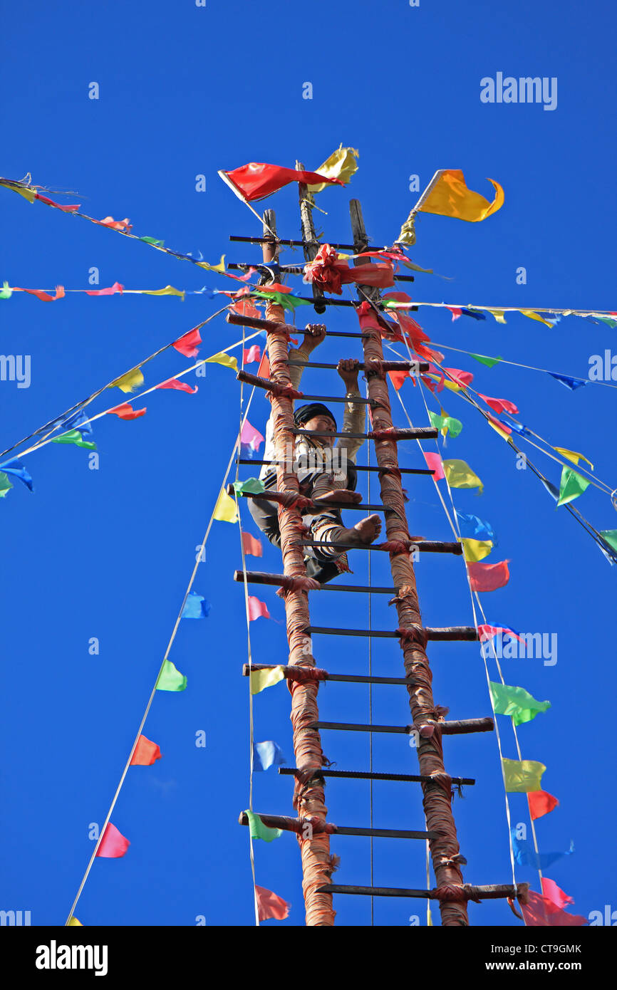 A barefooted Naxi ethnic man climbs the steps of a ladder made of sharp knives at the Dongba Valley Cultural Village in Lijiang Stock Photo