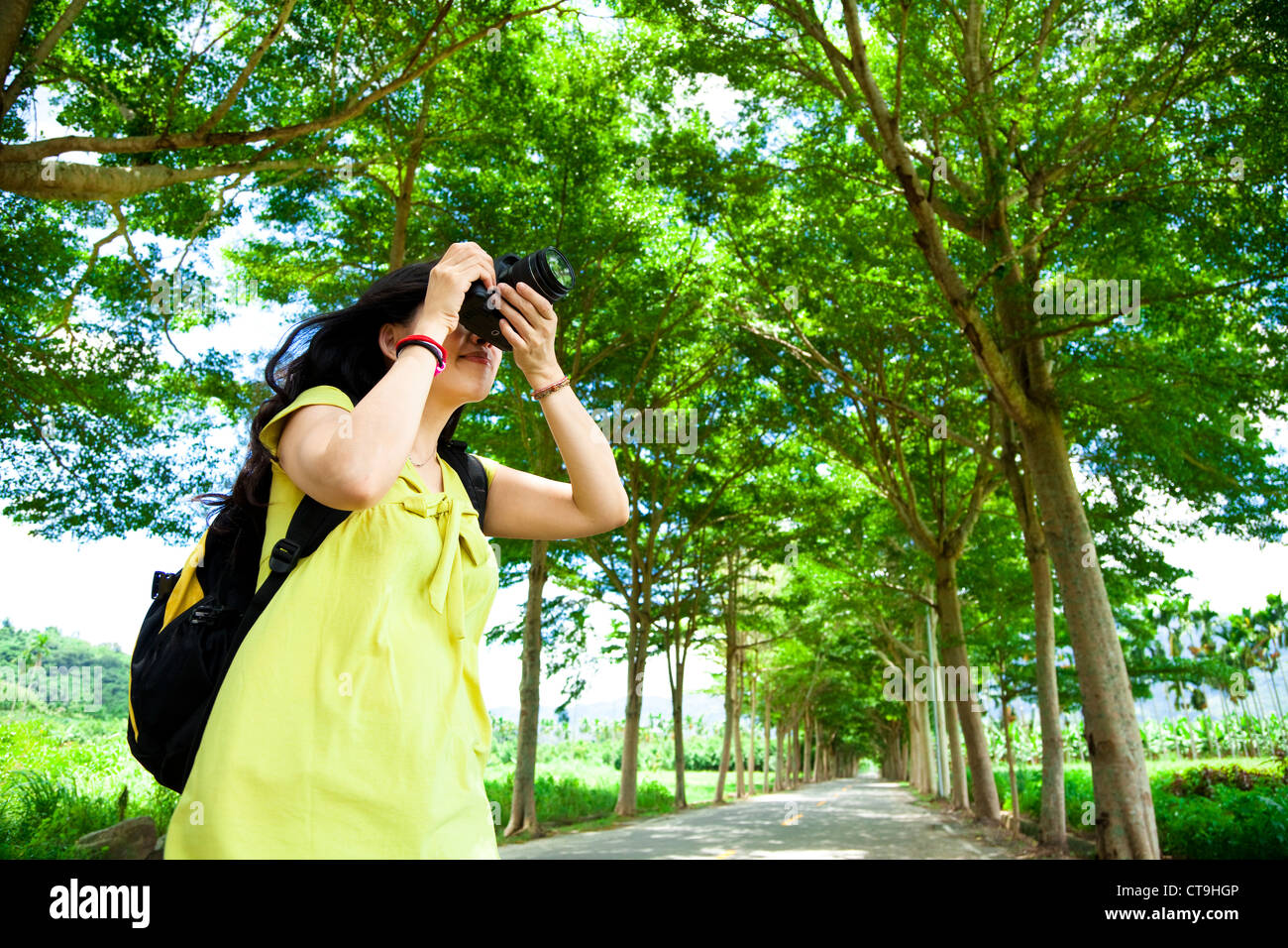 Young woman with backpack standing in the green forest taking photo Stock Photo