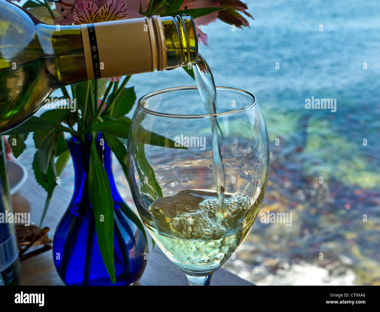 Pouring glass of white wine in alfresco coastal restaurant with sea and coast behind Stock Photo