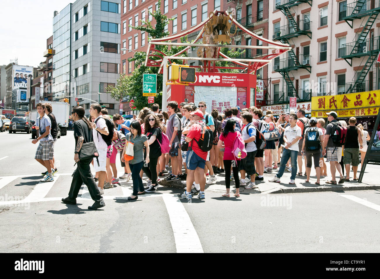 large tourist group of young people with adult supervision cross Canal street in front of Chinatown information kiosk New York Stock Photo