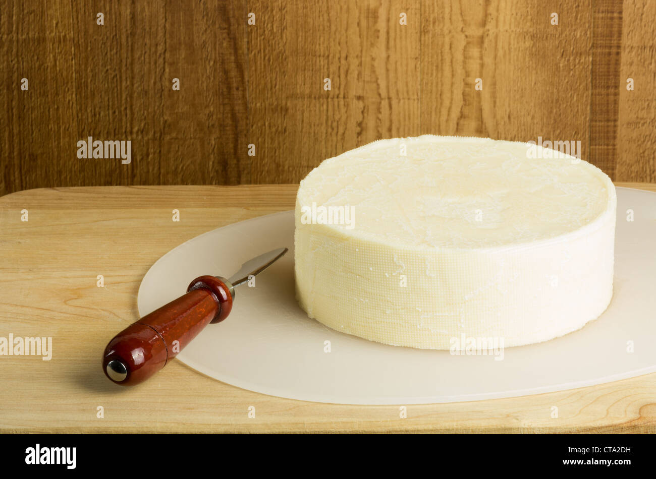 A round block of white cheddar cheese with a knife Stock Photo