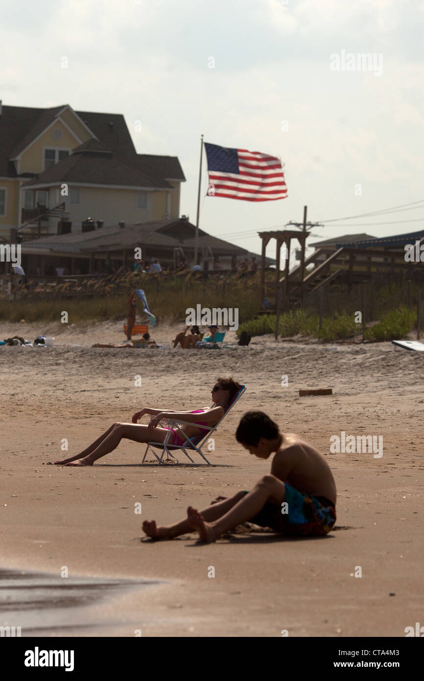 Tourists sunbathing  on Surf City beach , Topsail Island , North Carolina , USA with stars and stripes American flag Stock Photo