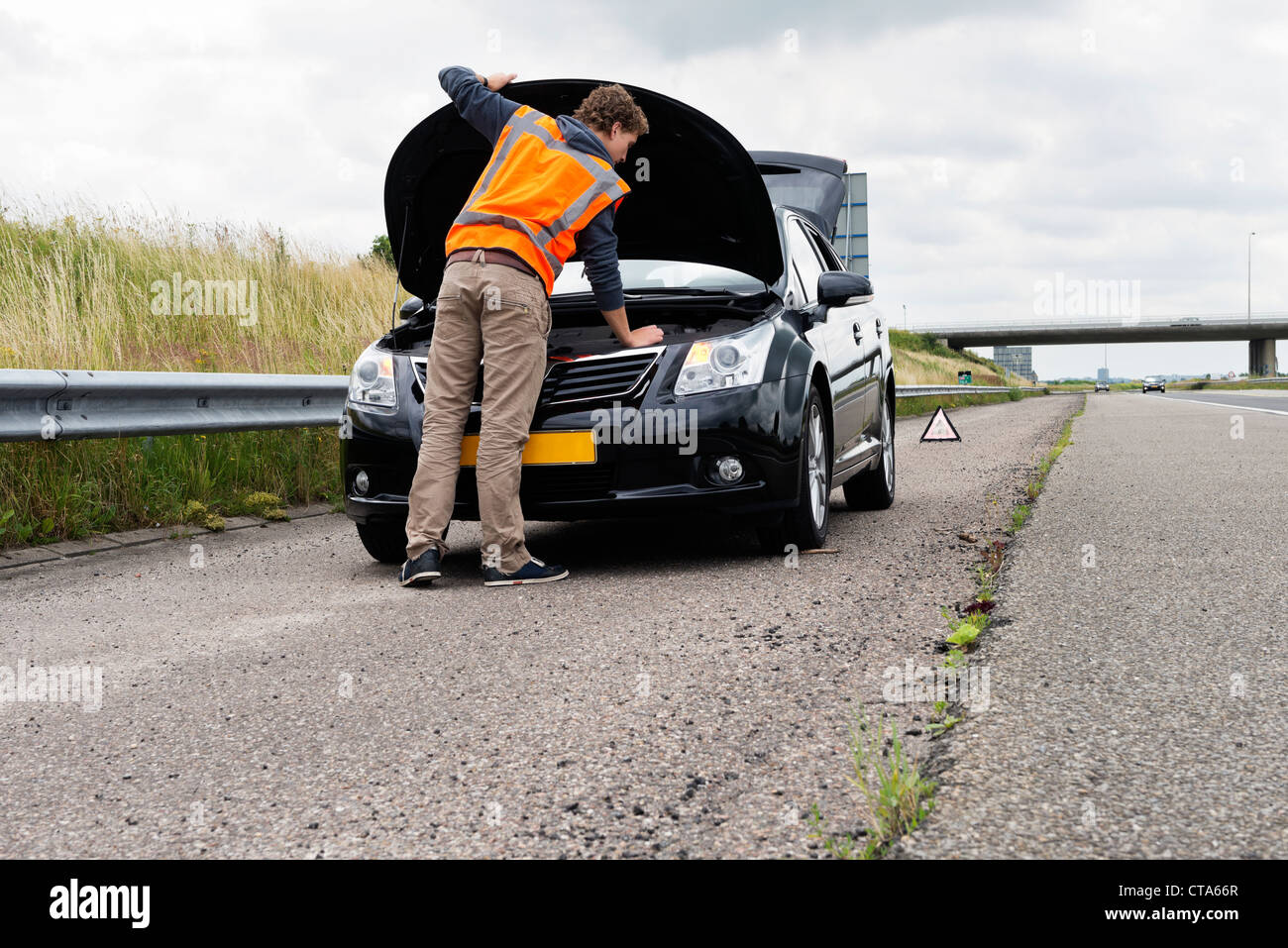 Stranded motorist attempting to fix his broken down car on the shoulder of a motorway Stock Photo