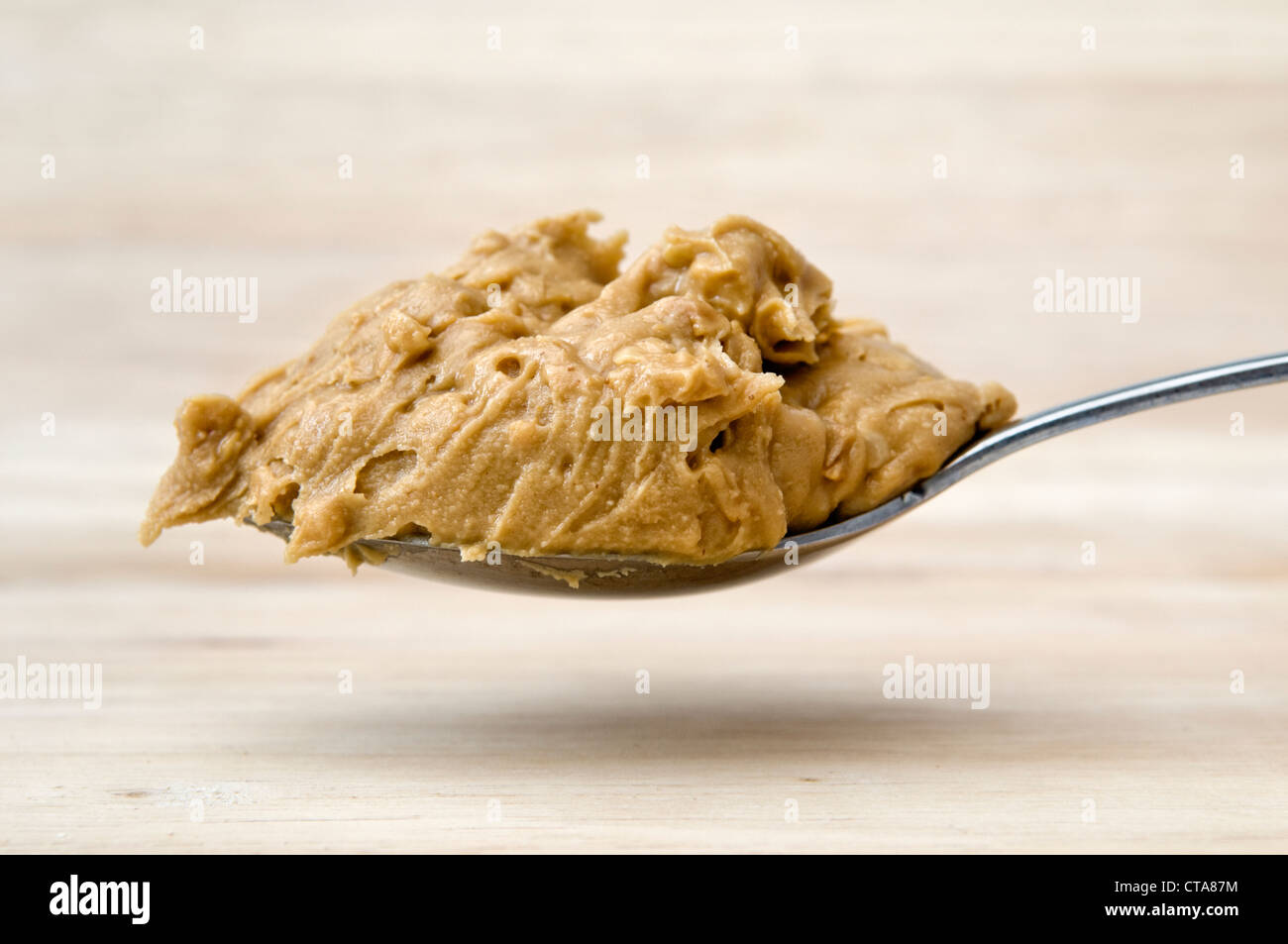https://c8.alamy.com/comp/CTA87M/heaped-spoon-of-peanut-butter-held-over-a-wooden-chopping-board-CTA87M.jpg