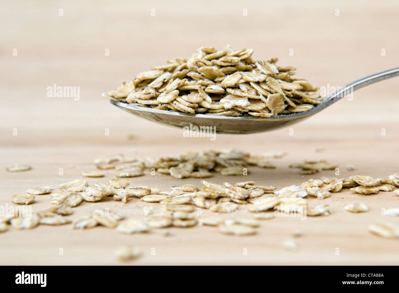 Heaped spoon of rolled oats overflowing onto a wooden chopping board