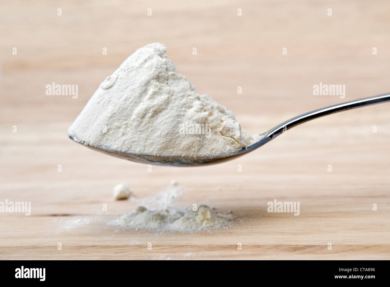 Heaped spoon of white flour overflowing onto a wooden chopping board Stock Photo