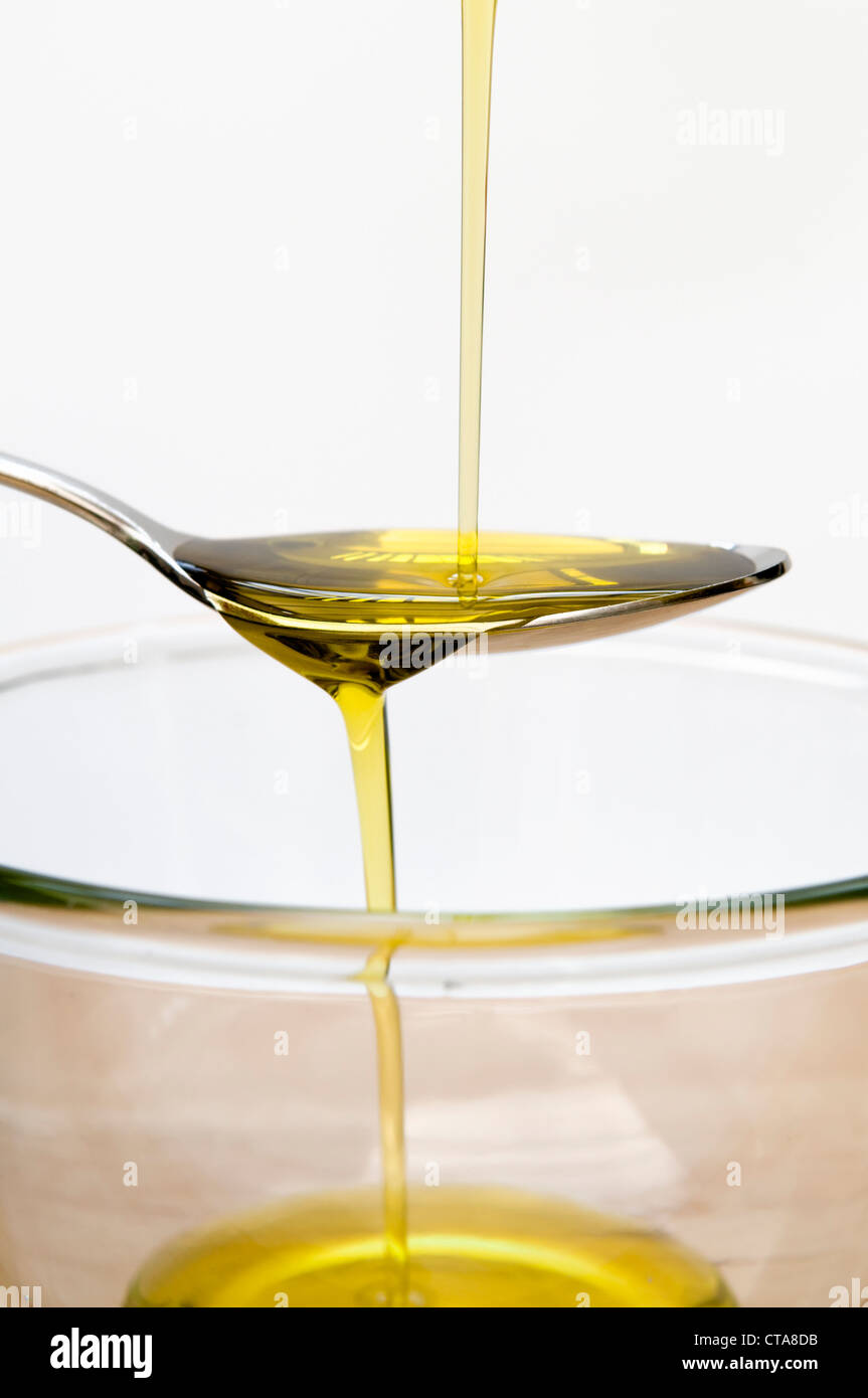 Olive oil being poured onto spoon over glass bowl Stock Photo Alamy