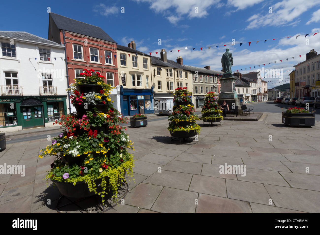 Municipal flower arrangements, Brecon town centre, with woman smoking on a bench under the statue of the Duke of Wellington Stock Photo