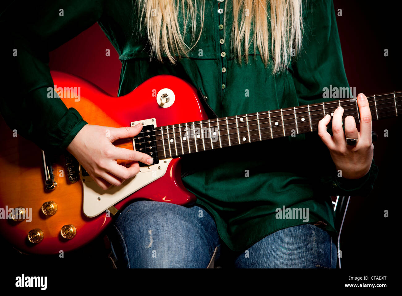 girl with a guitar on a dark red background Stock Photo - Alamy