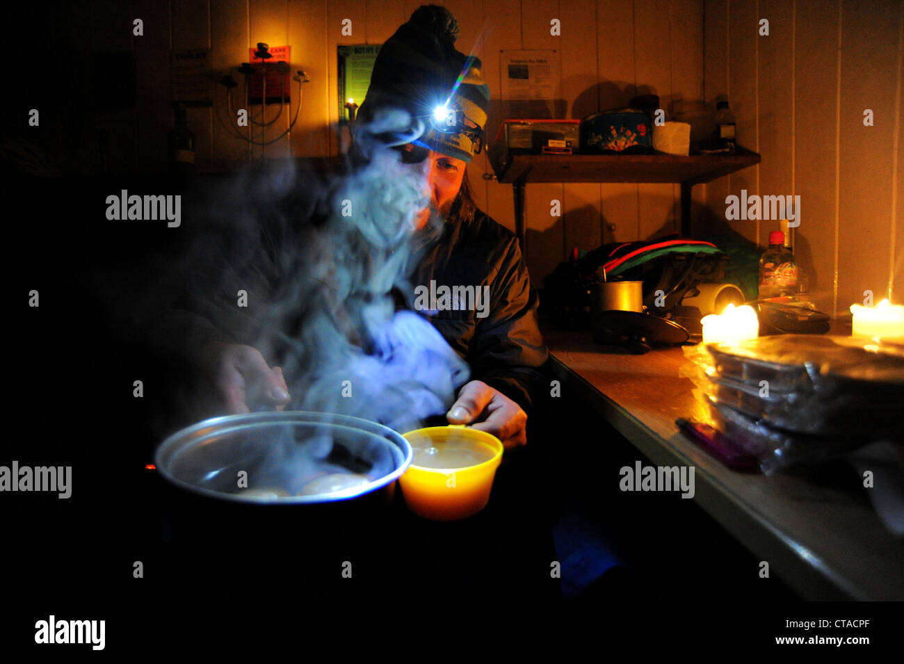 A man makes a cup of tea by candlelight in a bothy in the Scottish Highlands. Stock Photo