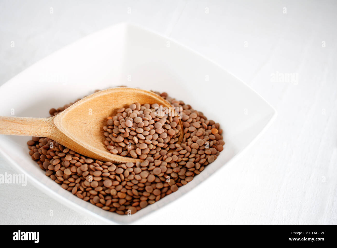 A bowl of brown lentils (Lens culinaris) with a wooden spoon Stock Photo