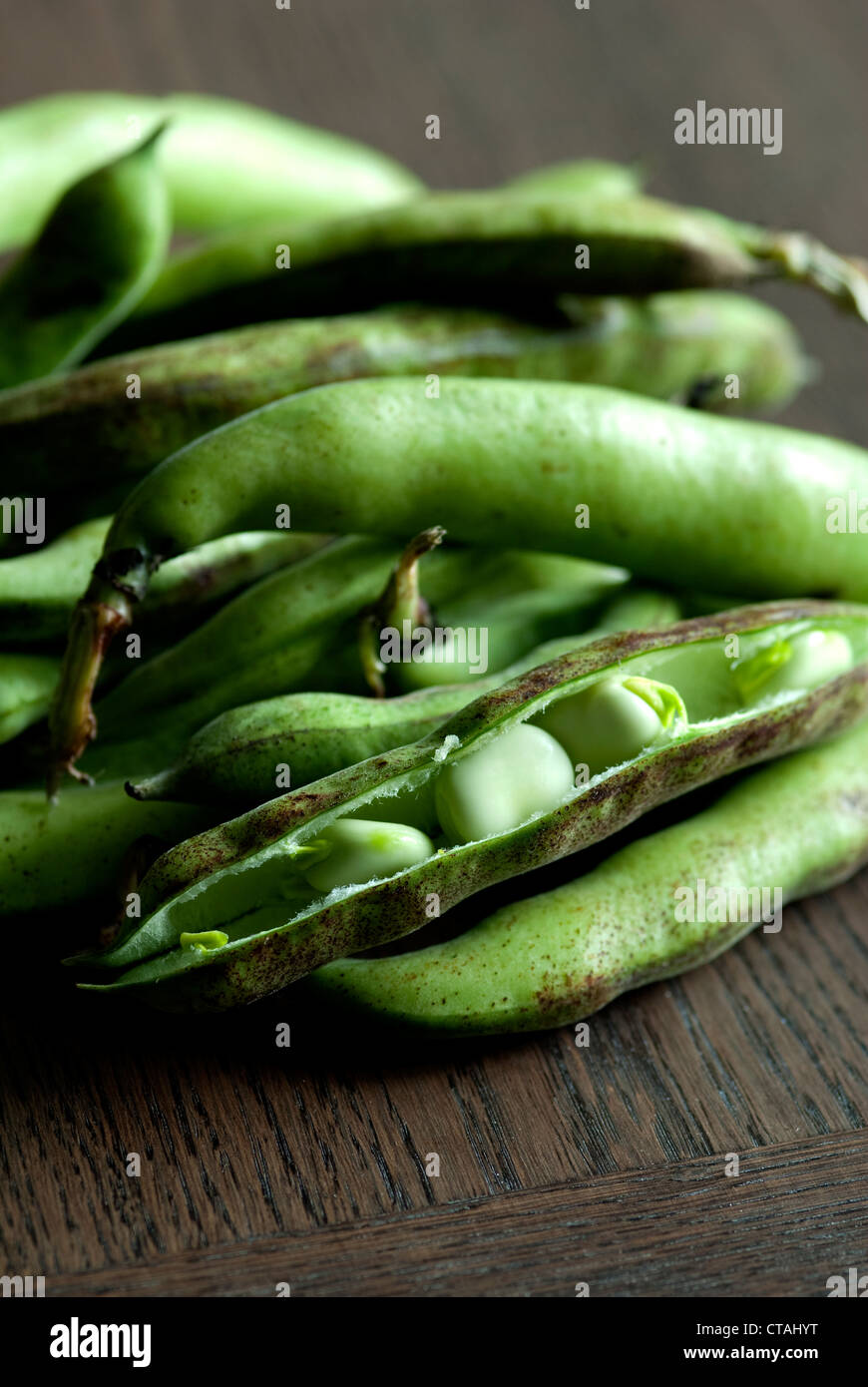 a close up image of green Broad beans pods with open pod showing beans