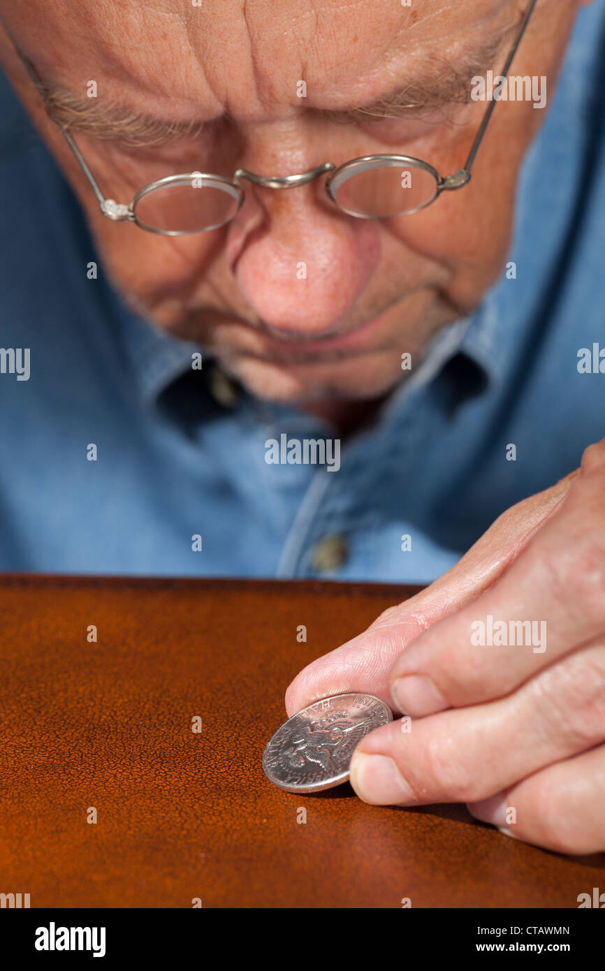 Senior retired caucasian man examining a half dollar coin through magnifying glasses Stock Photo