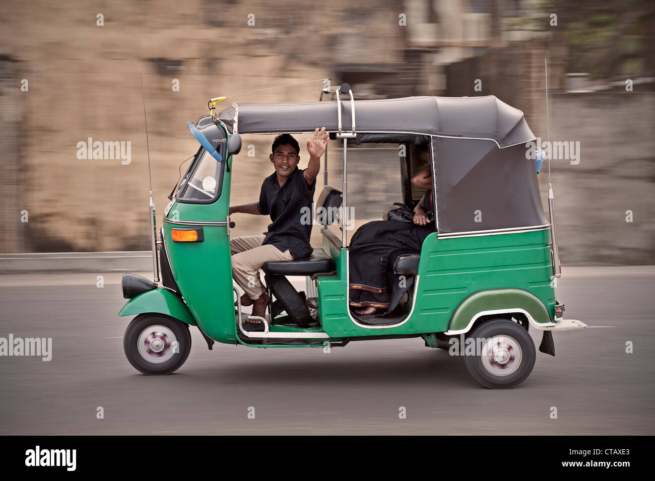 Local Tuk Tuk driver waves hello out of his three wheeler while passing by, capital Colombo, Sri Lanka Stock Photo