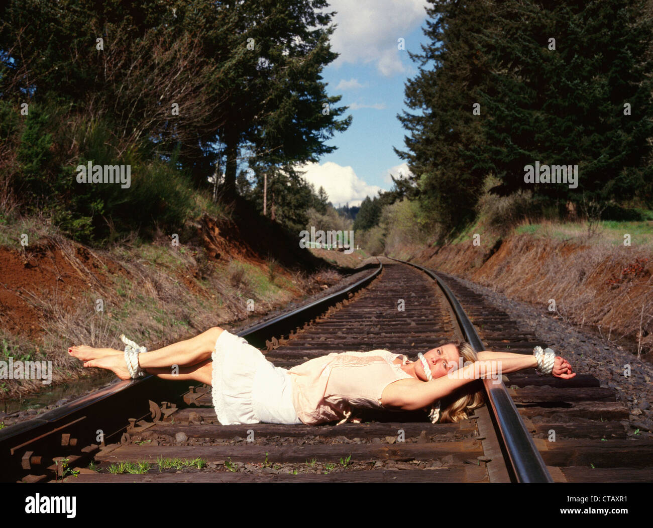 A woman tied on some railroad tracks like a 'damsel in distress.' Stock Photo