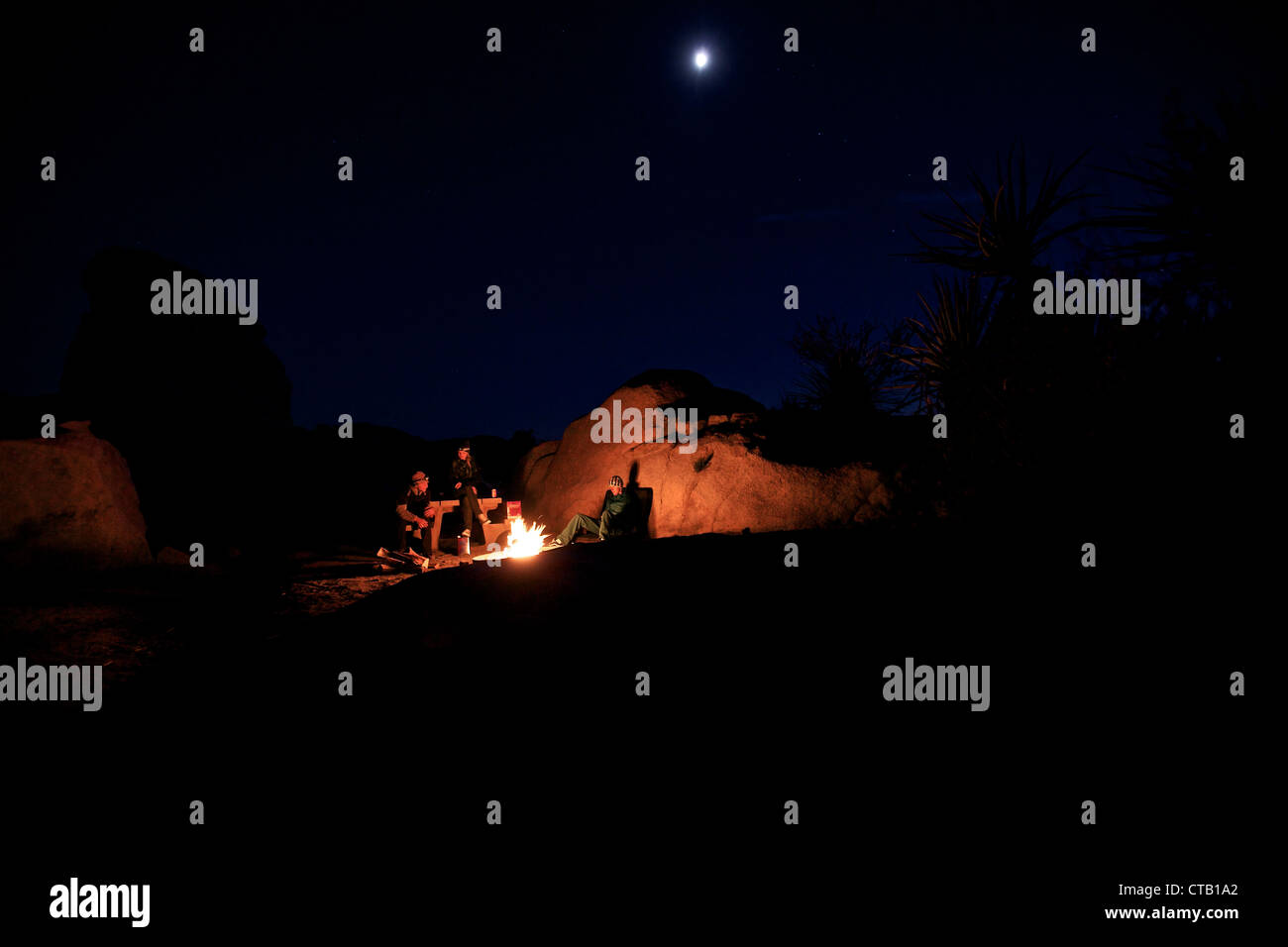 Three people sitting together around a campfire, Joshua Tree National Park, California, USA Stock Photo