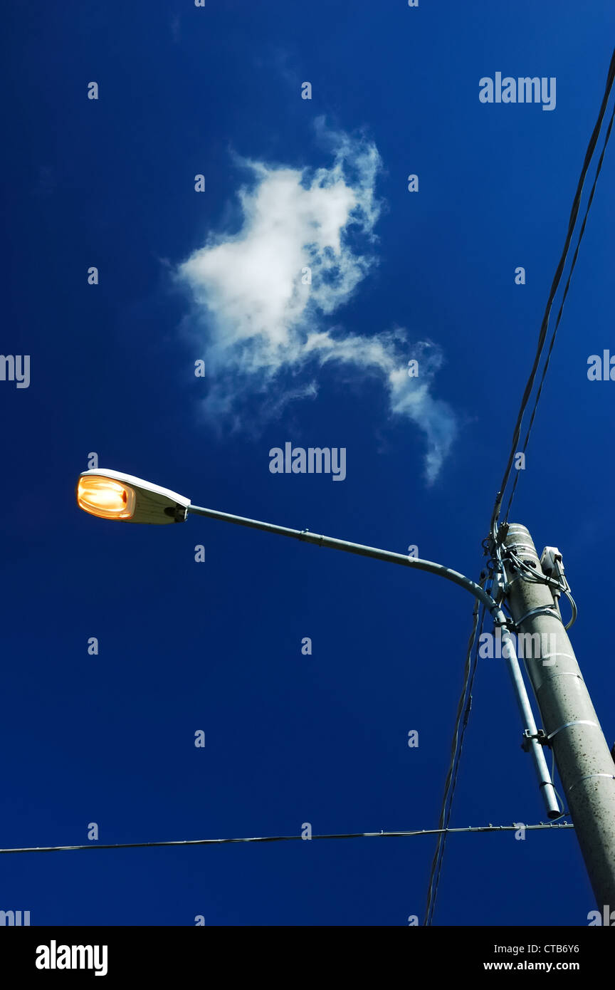 A street light on during the day, against a polarized blue sky Stock