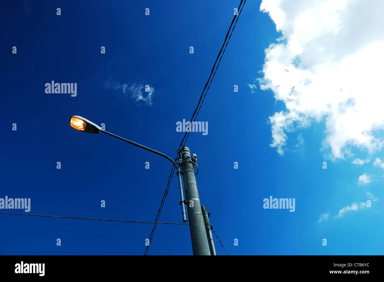 A street light on during the day, against a polarized blue sky Stock
