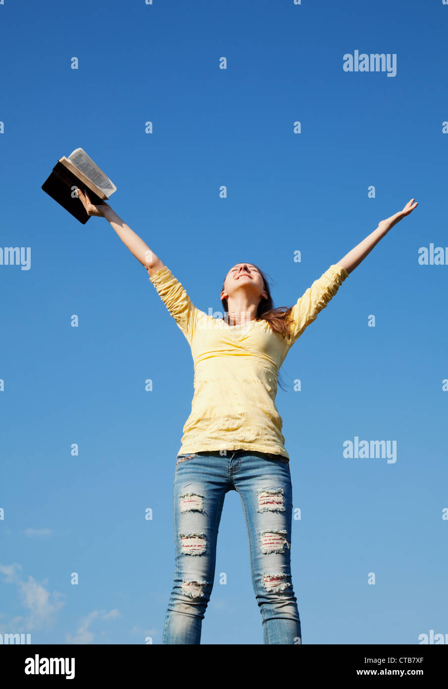 Young woman staying with raised hands against blue sky Stock Photo - Alamy