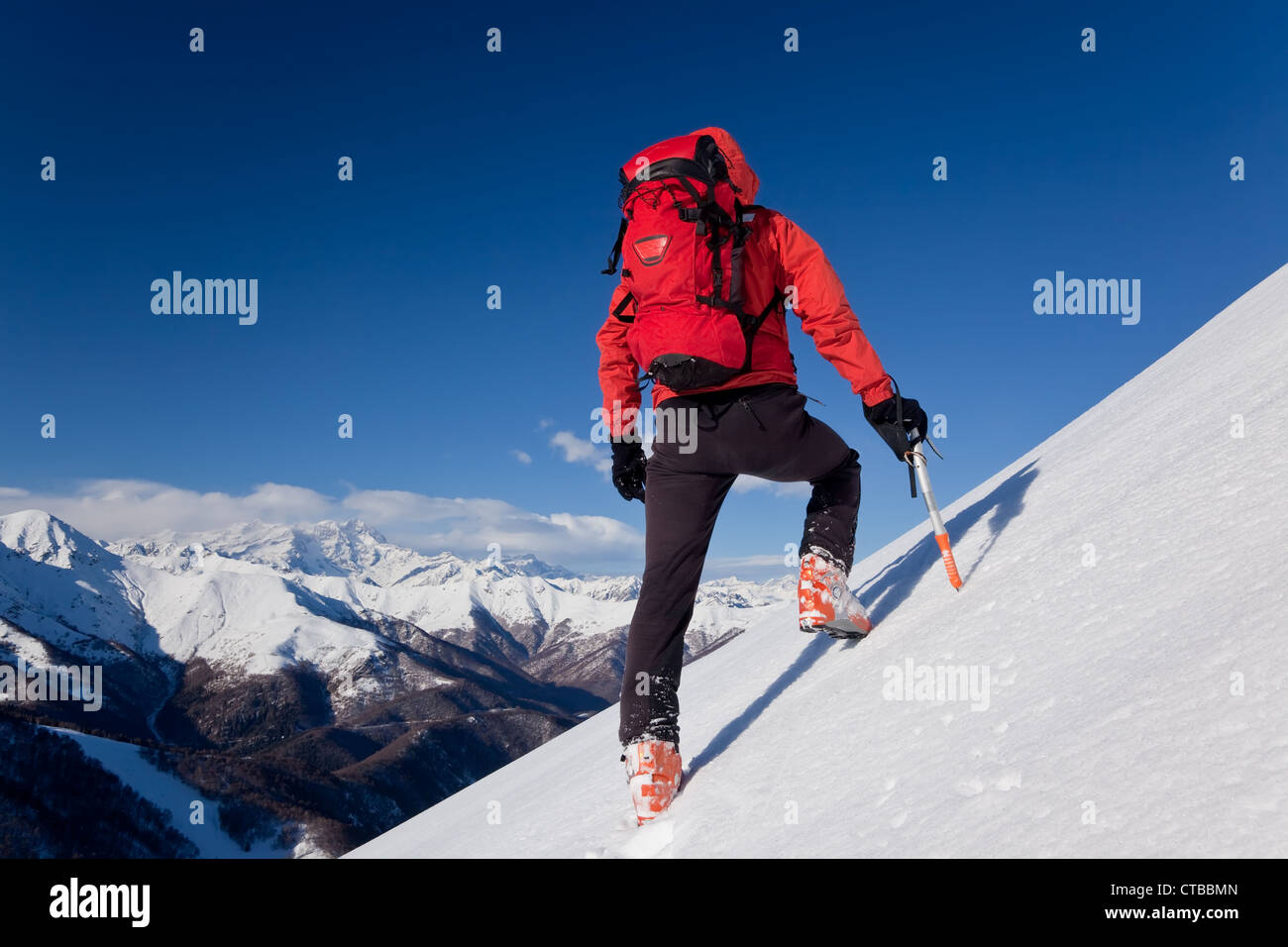 A male climber dressed in red climbs down snowy slope Winter clear sky day In background Monte Rosa massif Italy Europe Stock Photo
