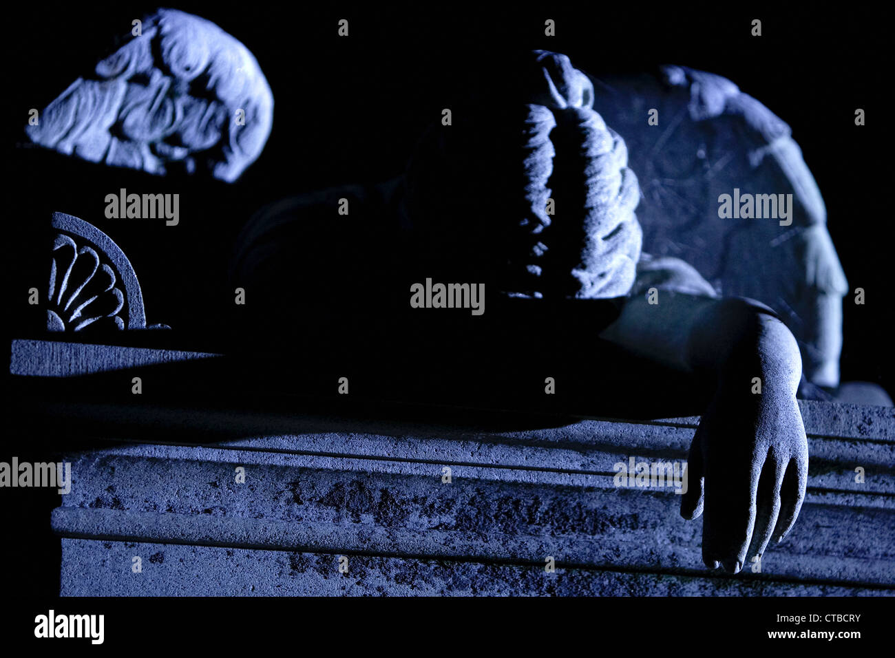 Stone sculpture of a fallen angel on top of a tomb in an historic Southern cemetery in blue moonlight Stock Photo