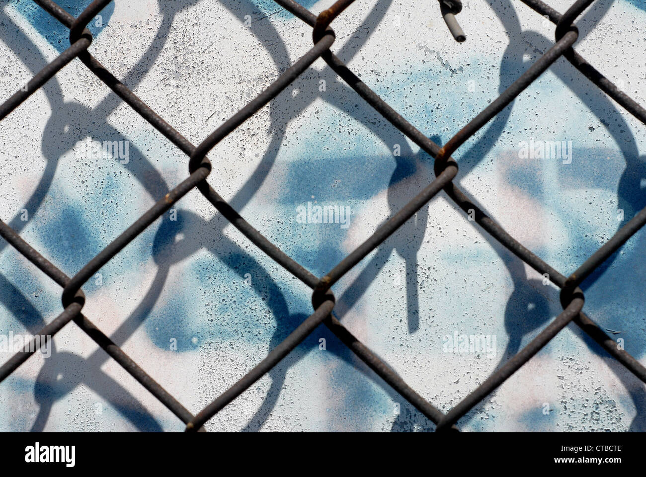 Close-up on a chain link fence against a white background with blue dripping spray paint Stock Photo