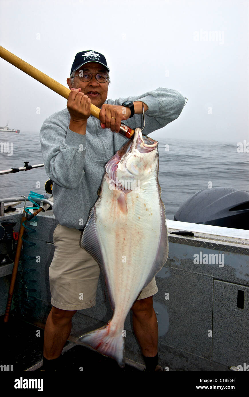 Asian ocean saltwater sport fishing angler holding big 'chicken' halibut flapping tail Swiftsure Bank Port Renfrew BC Stock Photo