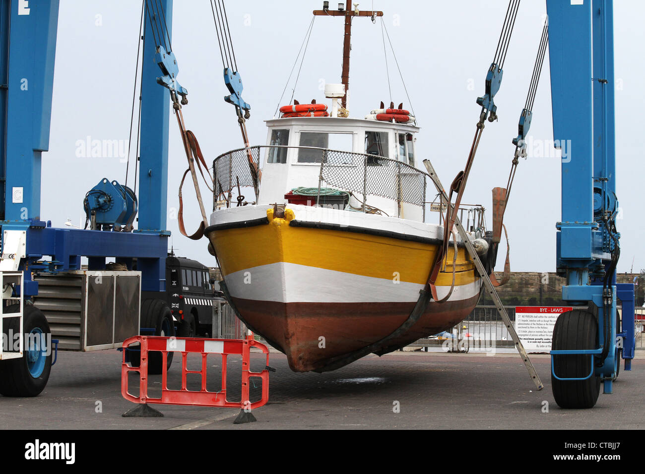 Boat in crane lift sling on harbor quay side for repair work. Stock Photo