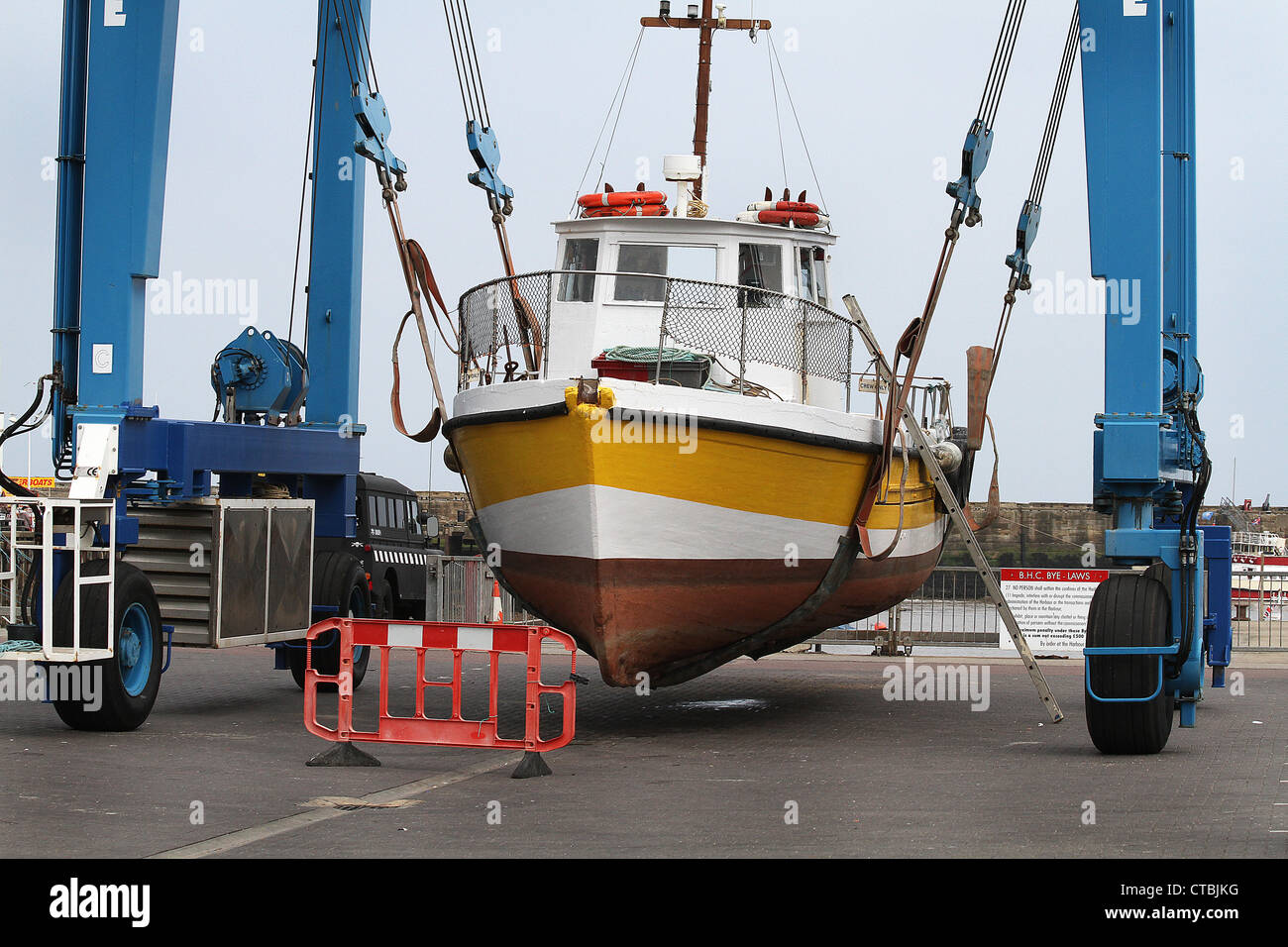 Boat in crane lift sling on harbor quay side for repair work. Stock Photo