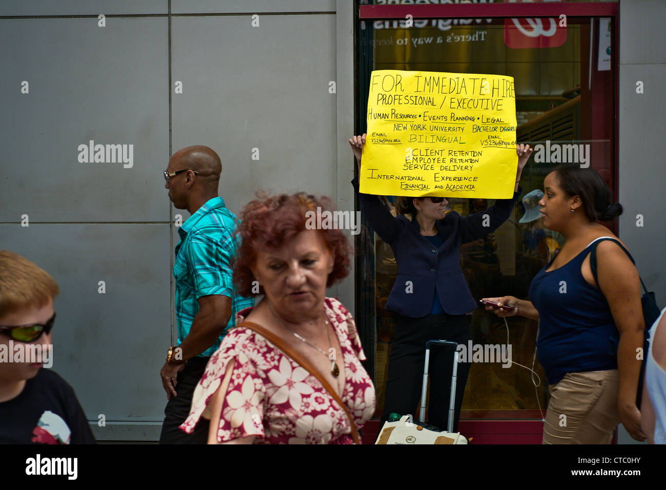 People pass by as Vilmarie Santos, who says she is unemployed, holds a sign seeking work, near Times Square, New York, NY, US Stock Photo