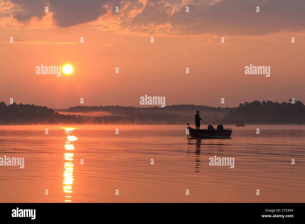 Fisherman in a boat silhouetted against a rising sun. Stock Photo