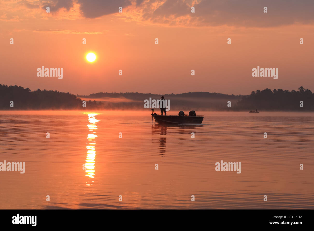 Fisherman in a boat silhouetted against a rising sun. Stock Photo
