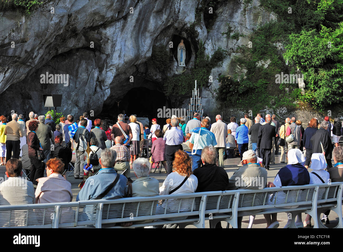 Pilgrims praying in front of the grotto at the Sanctuary of Our Lady of Lourdes, Pyrenees, France Stock Photo