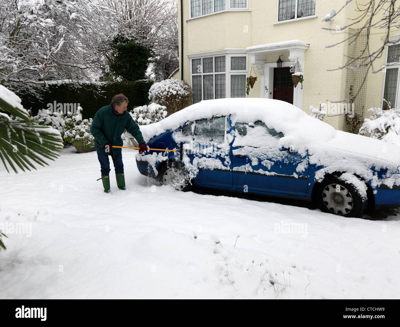 Man Using A Rubber Wonder Broom To Clear The Ice And Snow Off A Car During Winter Surrey England Stock Photo