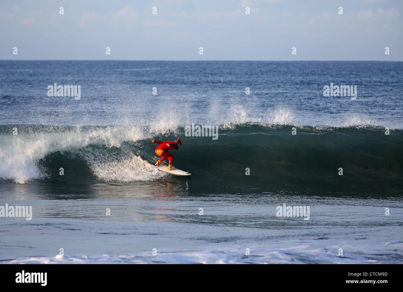 Bearded man surfing a wave wearing red superhero costume. Stock Photo