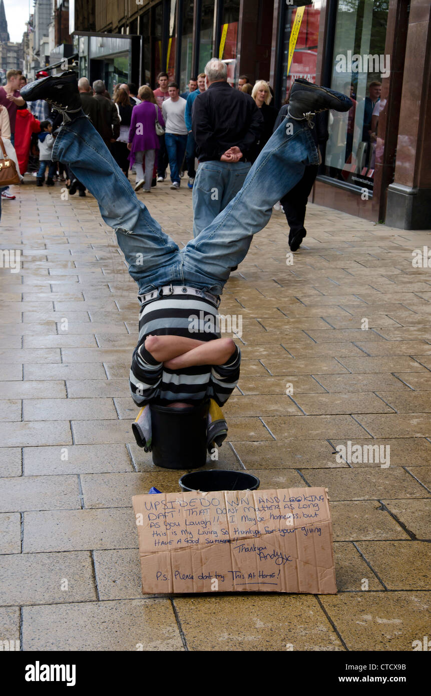 Man doing a head-stand with his head in a bucket in Princes Street, Edinburgh, Scotland. Stock Photo
