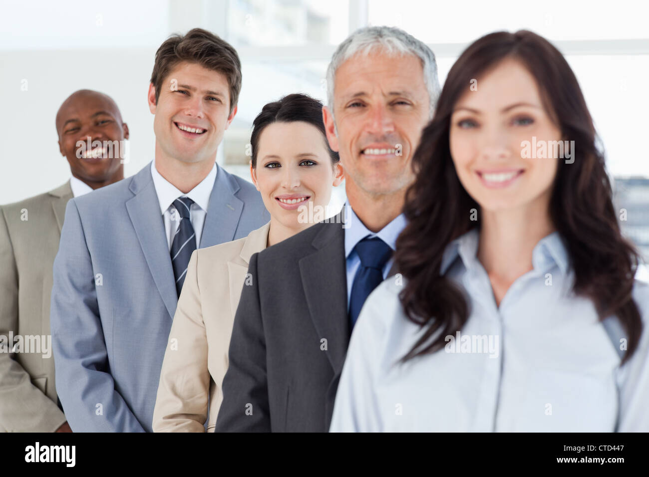 Young smiling executive standing in a well-lit room among his co-workers Stock Photo