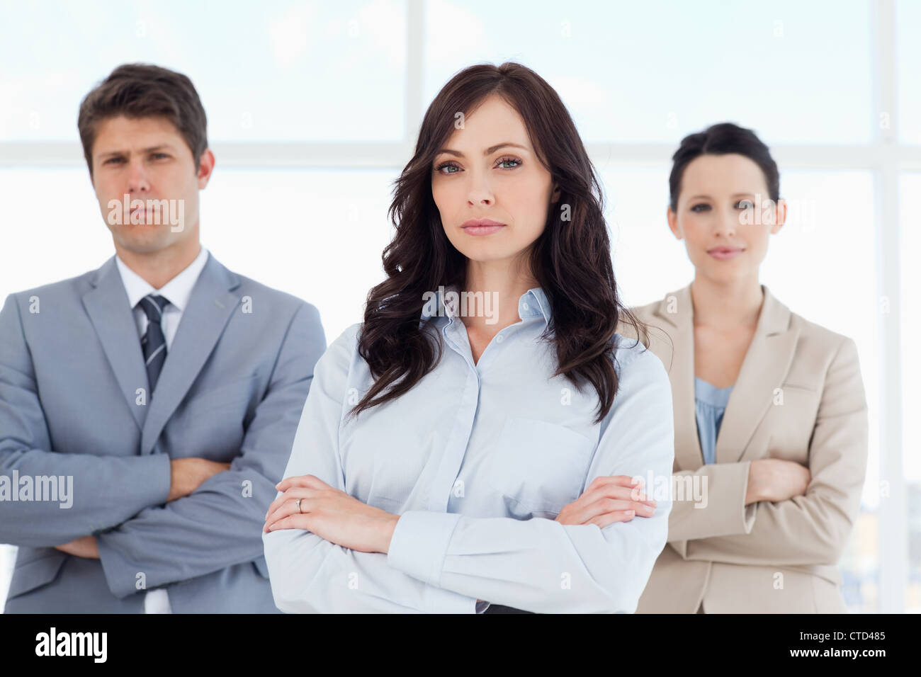 Three serious business people crossing their arms in a well-lit room ...