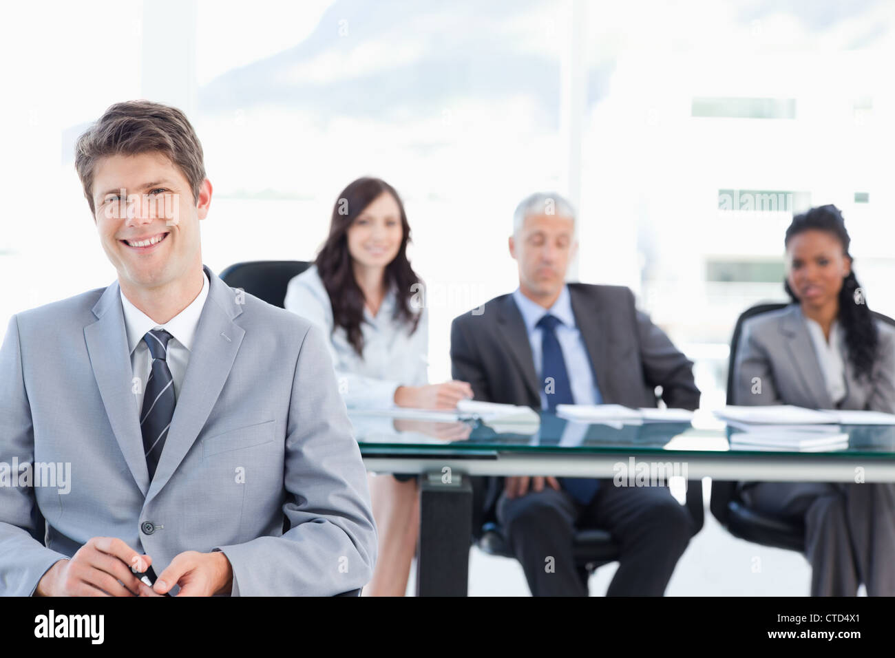 Smiling young businessman sitting in front of his team and looking at ...