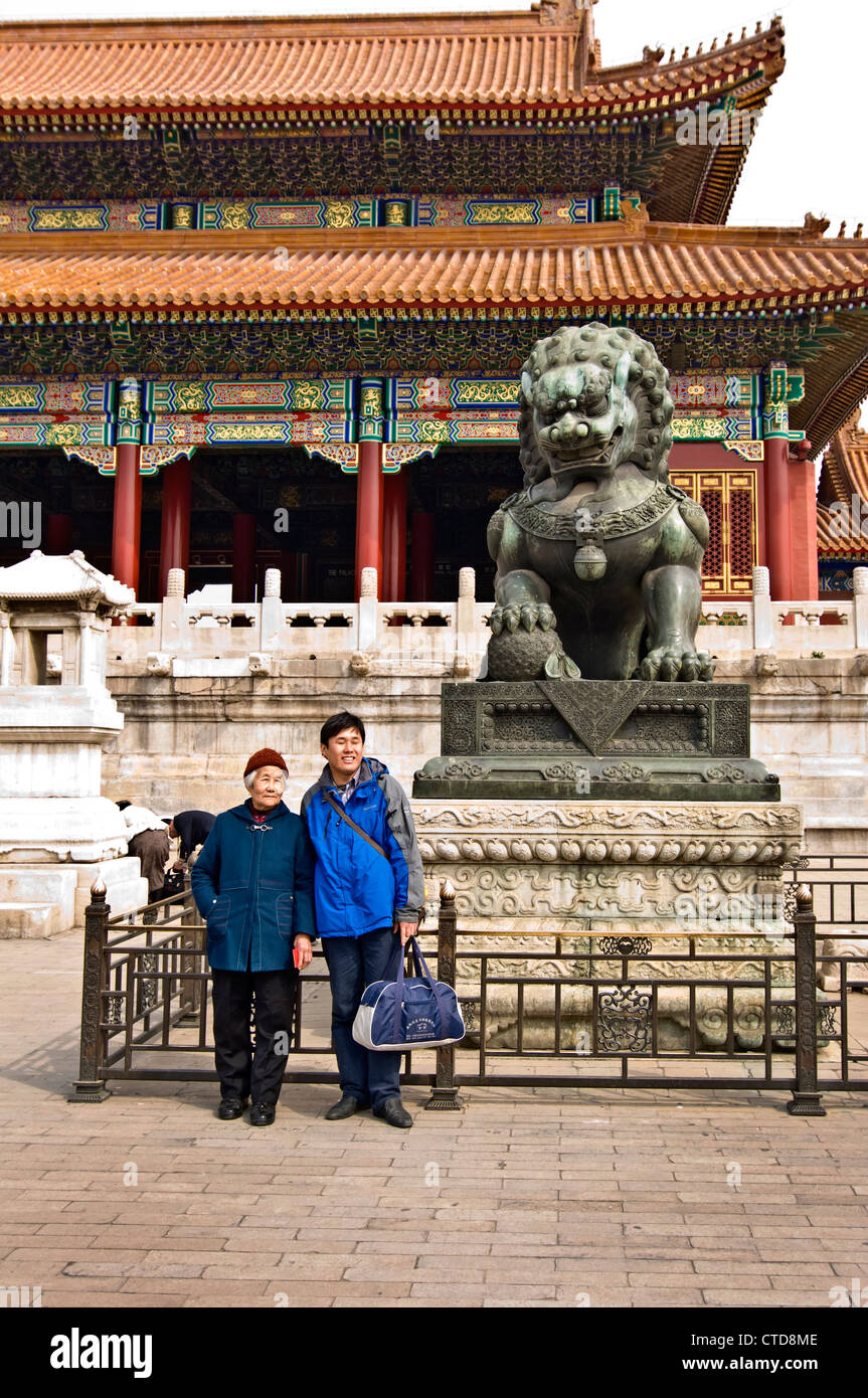 Two chinese tourists posing in front of the lion at the gate of Supreme harmony in the Forbidden City - Beijing, China Stock Photo