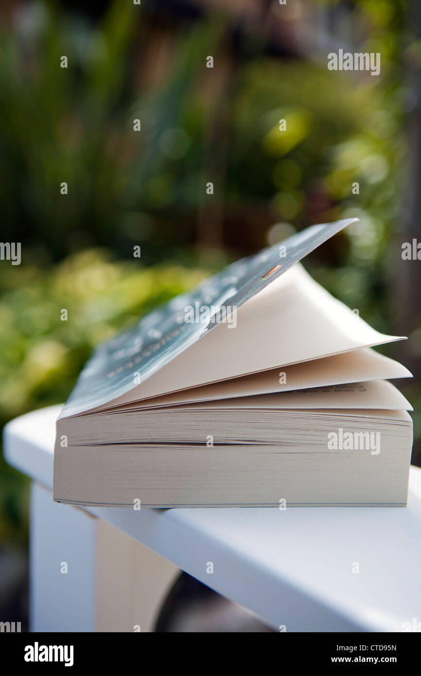 Open book resting on the arm of a garden chair.Shallow focus image. Stock Photo