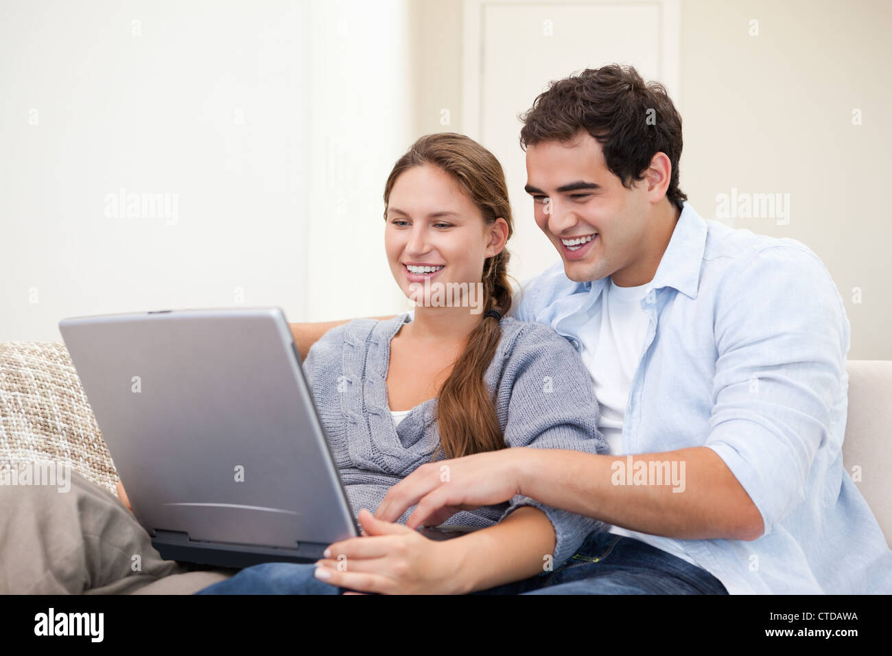 Couple sitting on a sofa while holding a laptop Stock Photo - Alamy